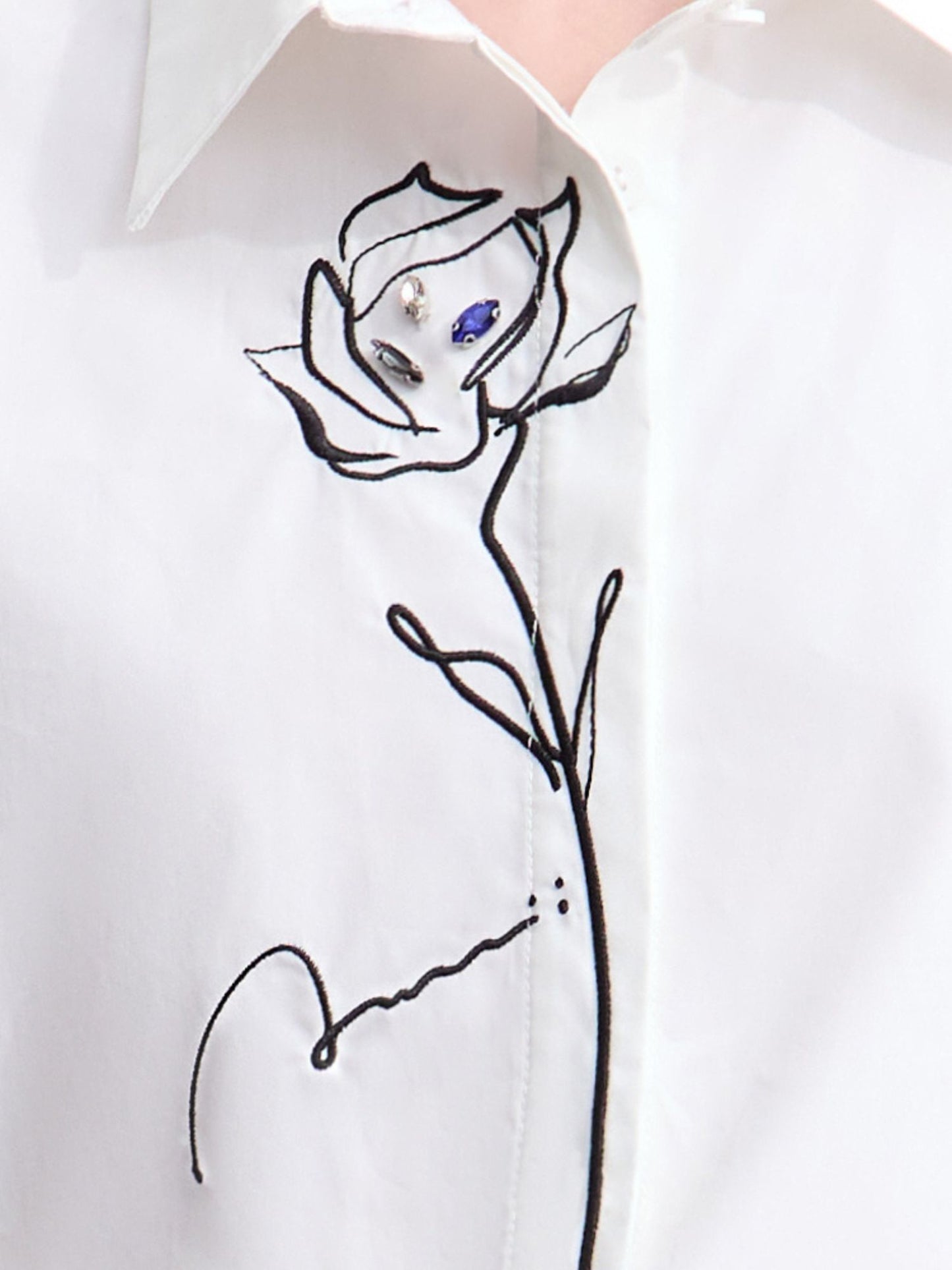 Nærbillede af blomstermotiv broderet på hvid skjorte.