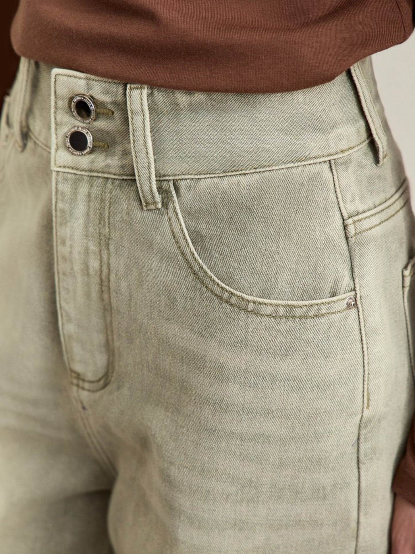 Frontvisning af jeans med diskrete slidmærker og synlig knaplukning.