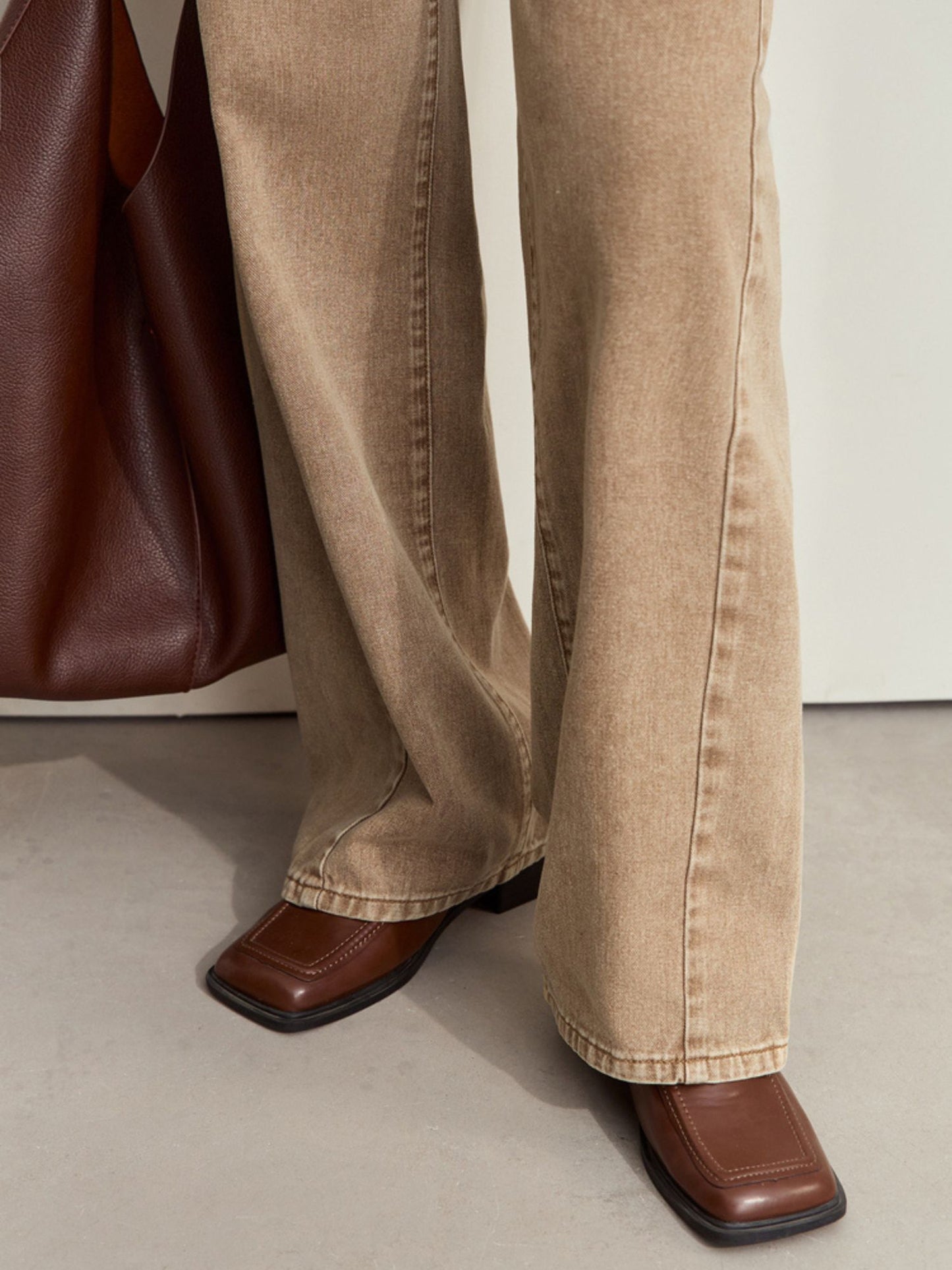 Nærbillede af ben og sko med beige bukser og brun taske.