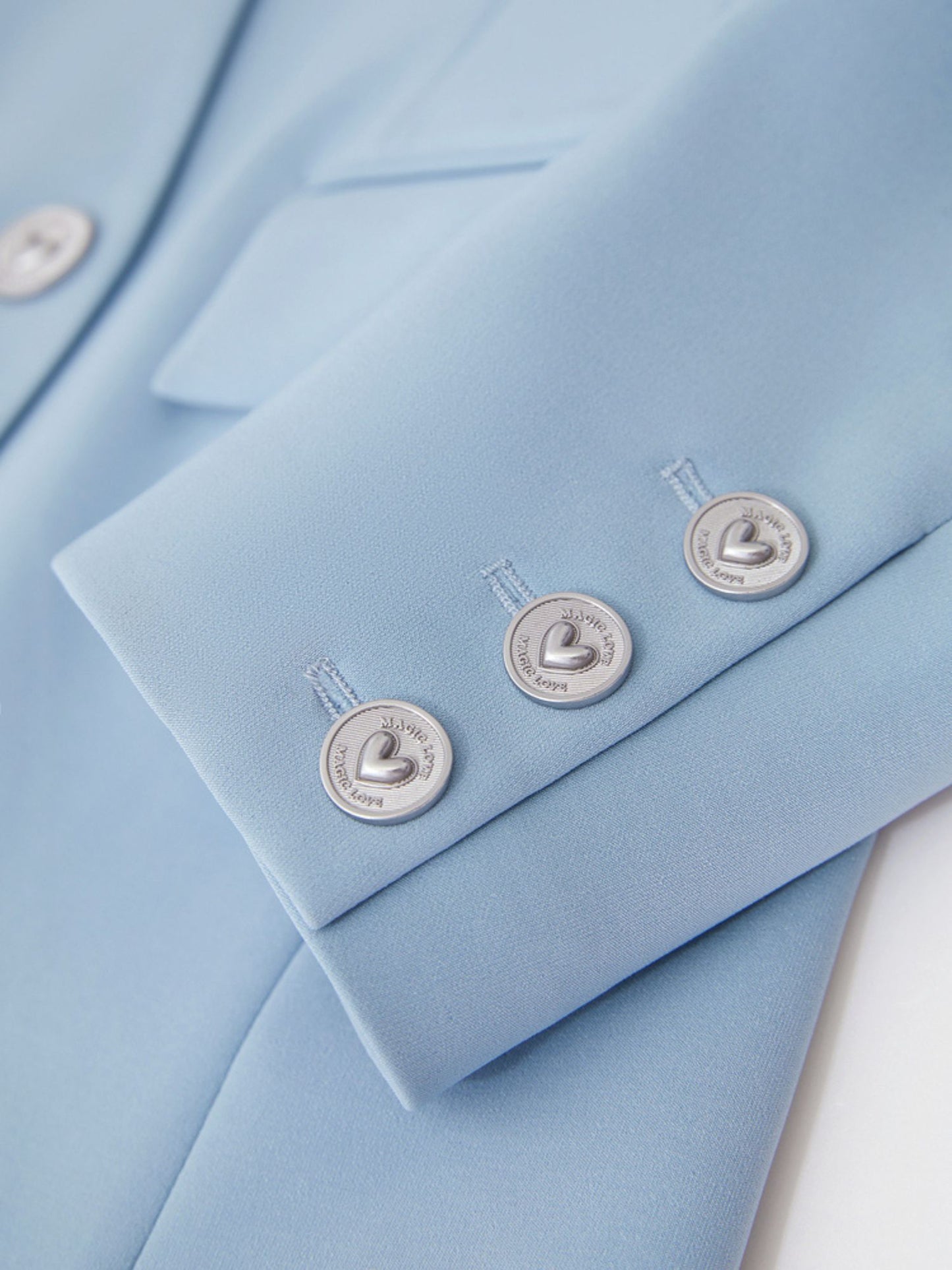 Nærbillede af lyseblå blazers sølvknapper og stoftekstur.