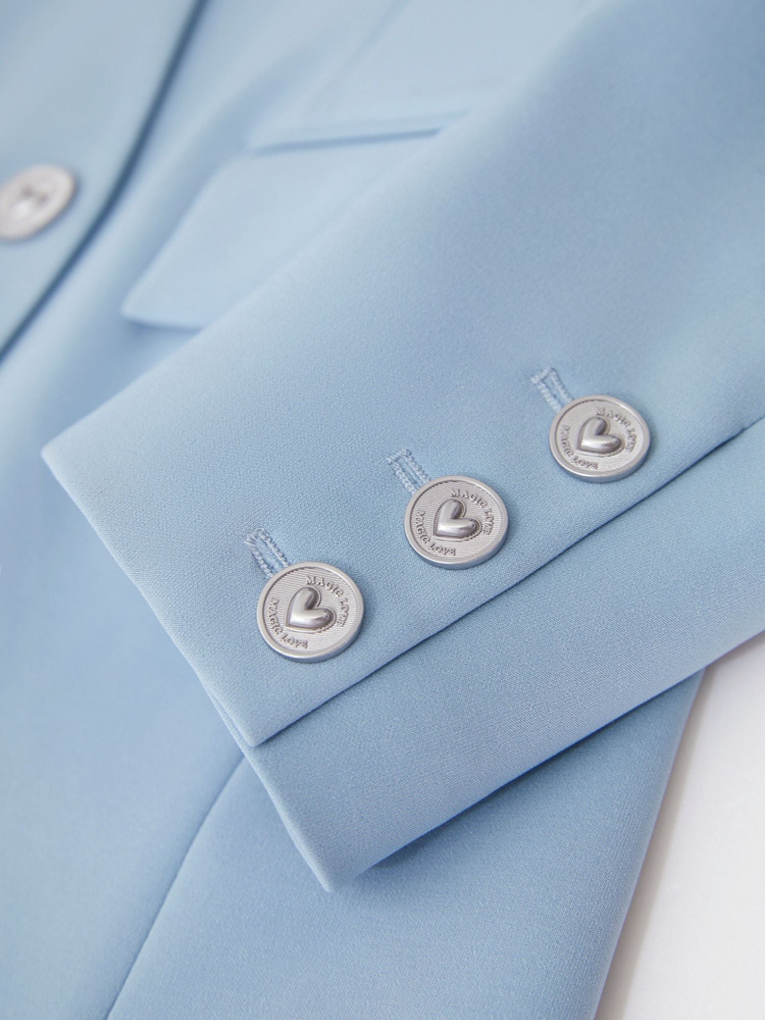 Nærbillede af lyseblå blazers sølvknapper og stoftekstur.