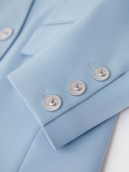 Nærbillede af lyseblå blazers sølvknapper og stoftekstur.