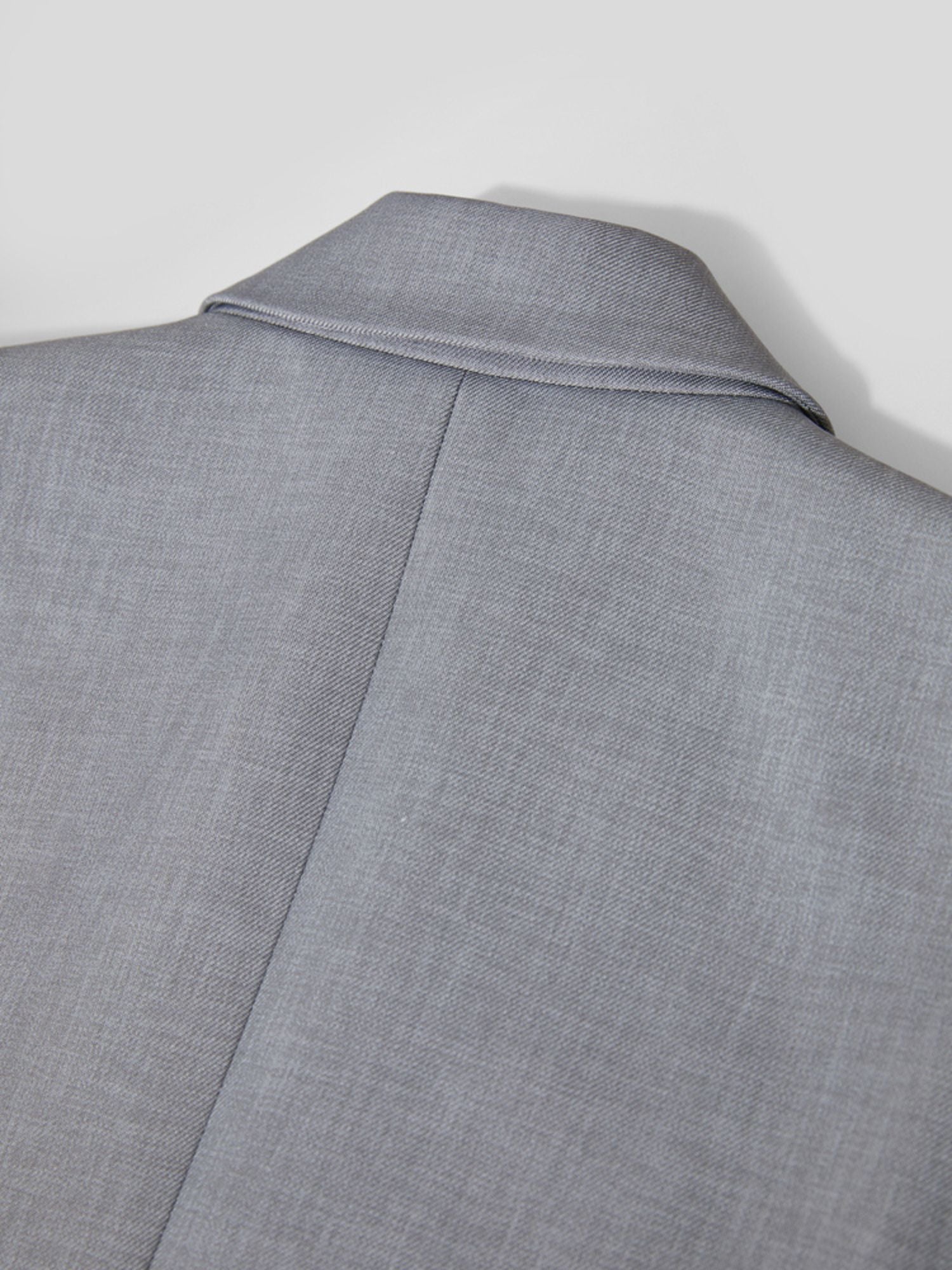 Detaljebillede af knaphul og syninger på grå blazer.