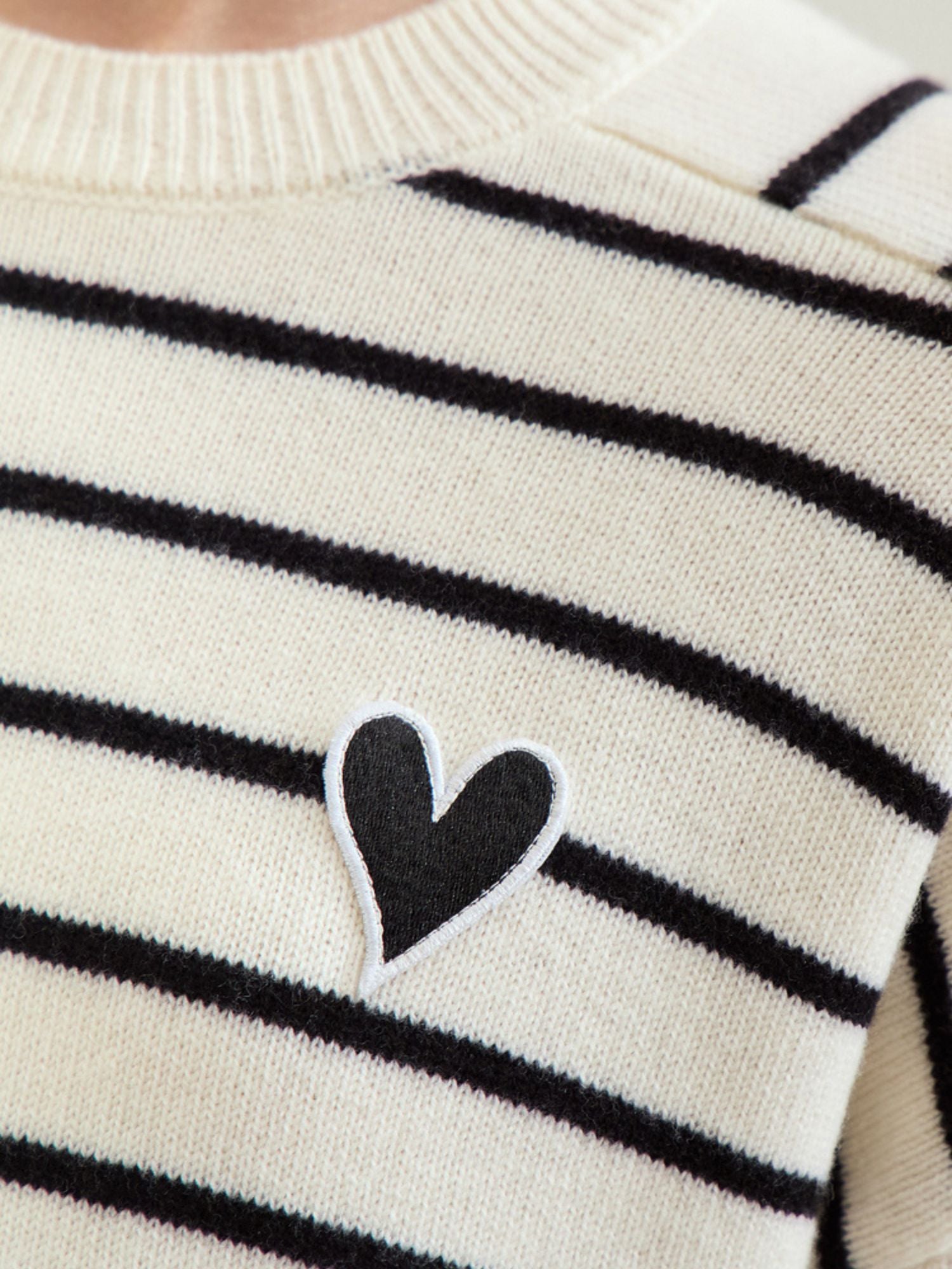 Nærbillede af mørkeblåt hjertebroderi på sort og hvid stribet sweater.