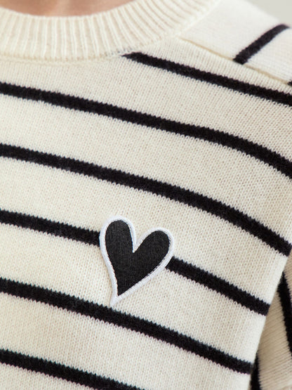 Nærbillede af mørkeblåt hjertebroderi på sort og hvid stribet sweater.