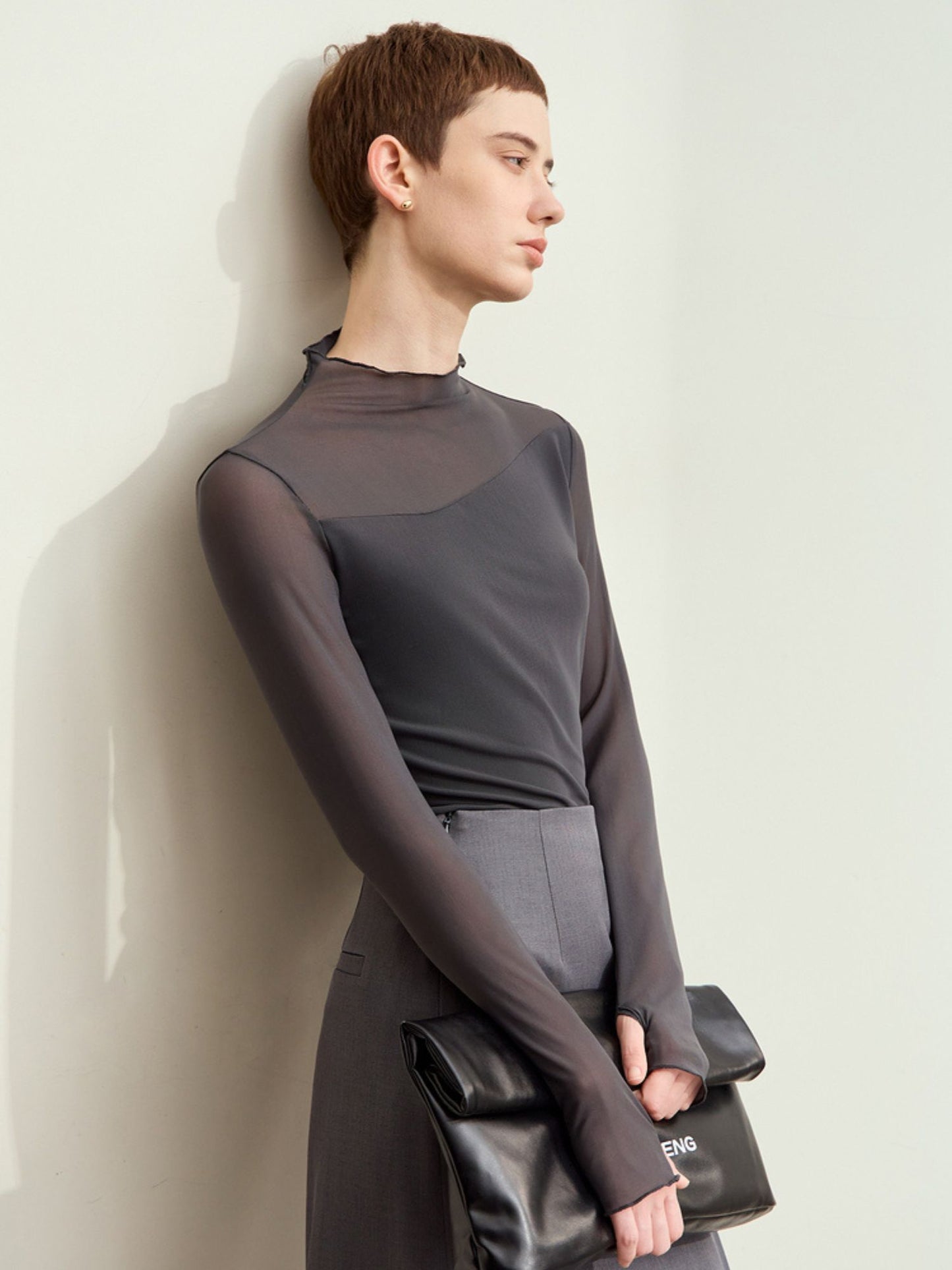 Grå mesh-bluse med sorte detaljer og lange ærmer, model står op ad væg.