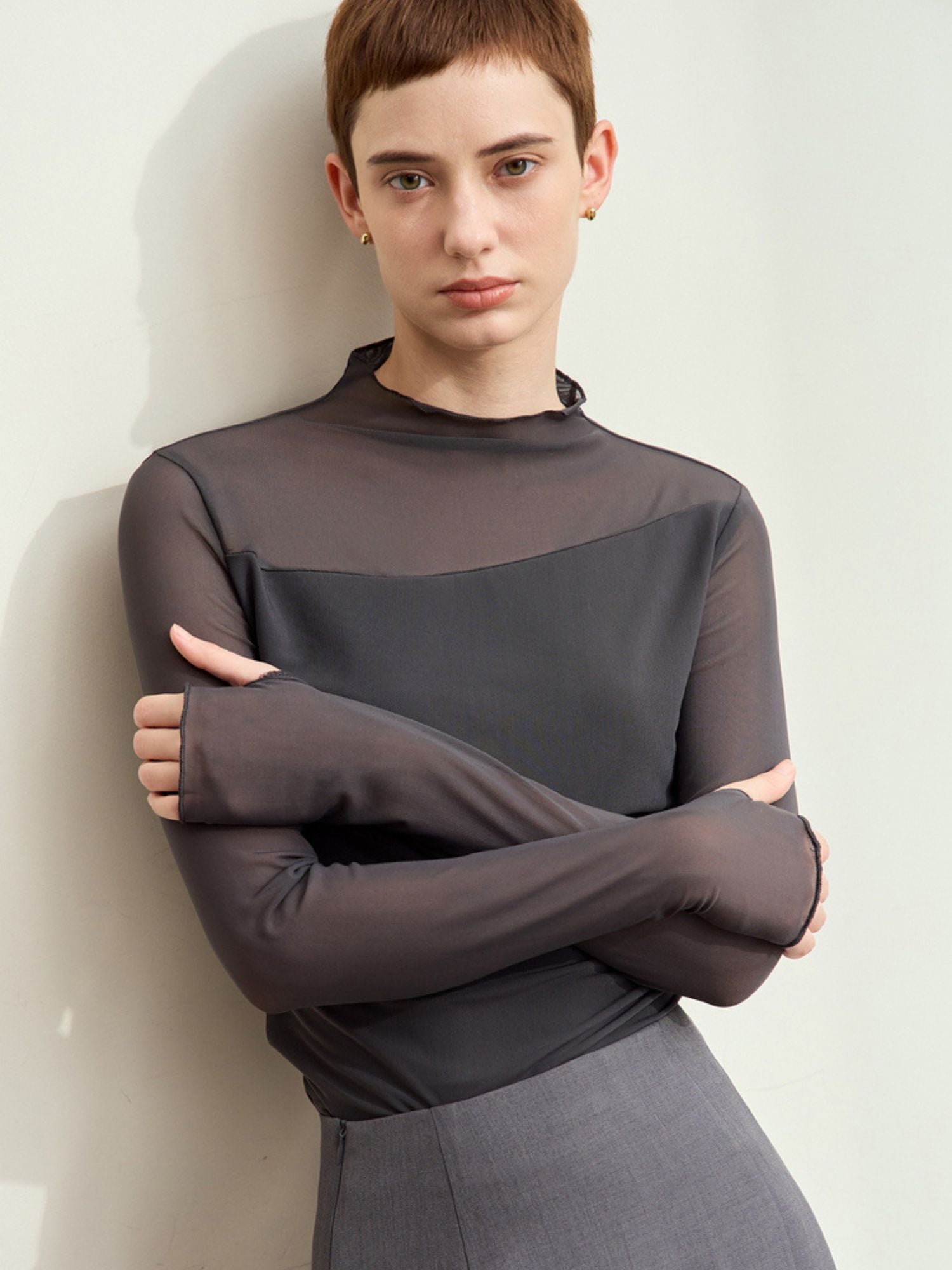 Skrå vinkel af grå mesh-bluse med synlig sort underdel og clutch.