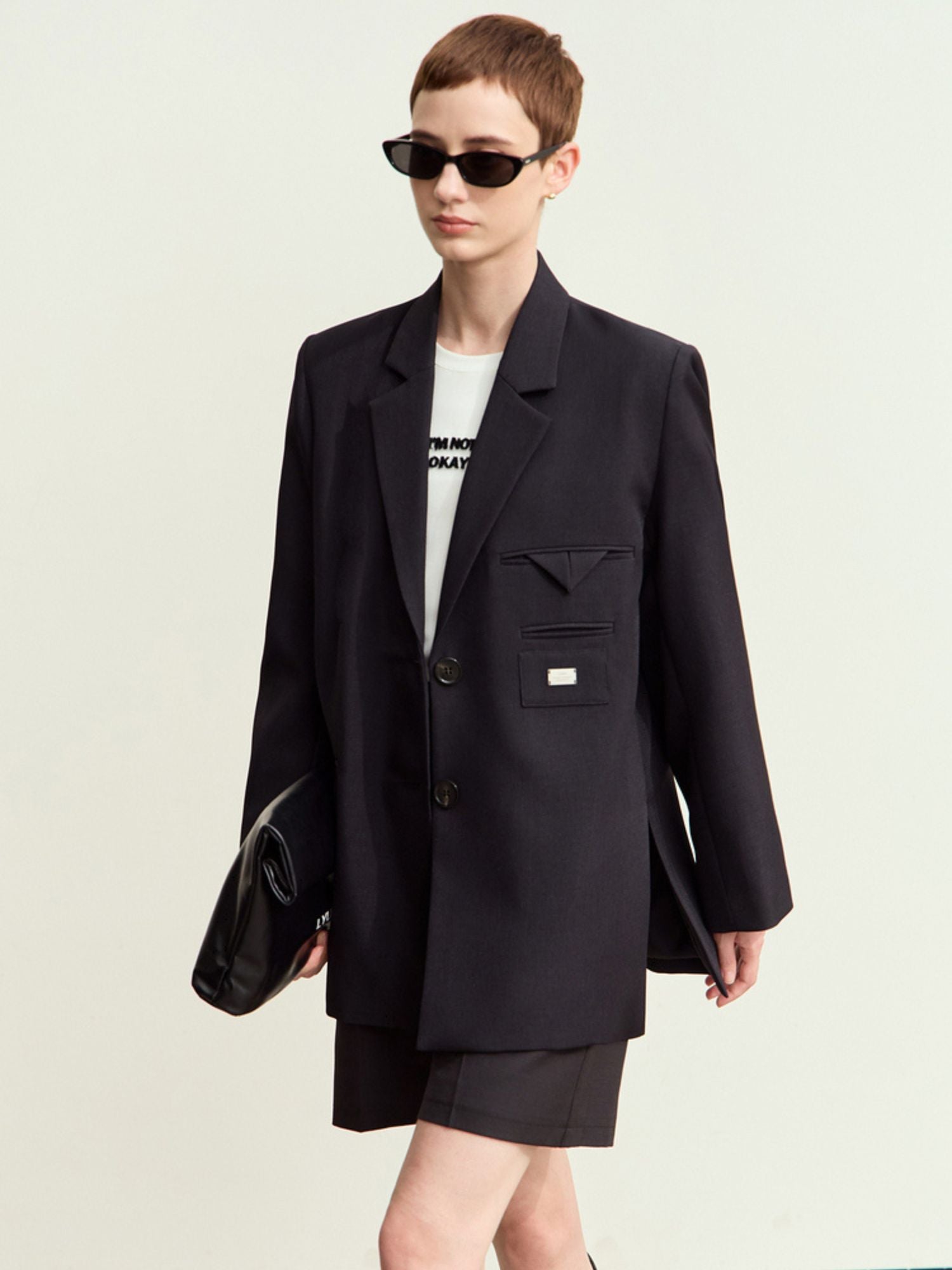 Frontvisning af sort blazer og nederdel med solbriller.