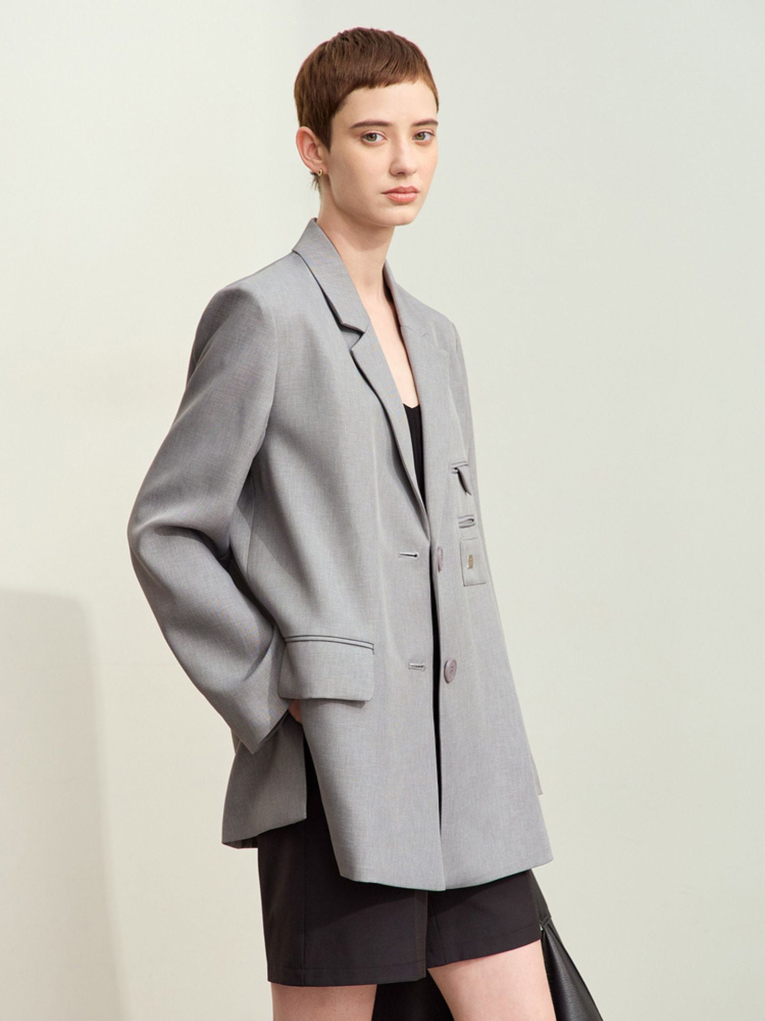 Model iført oversized grå blazer over sort mininederdel.