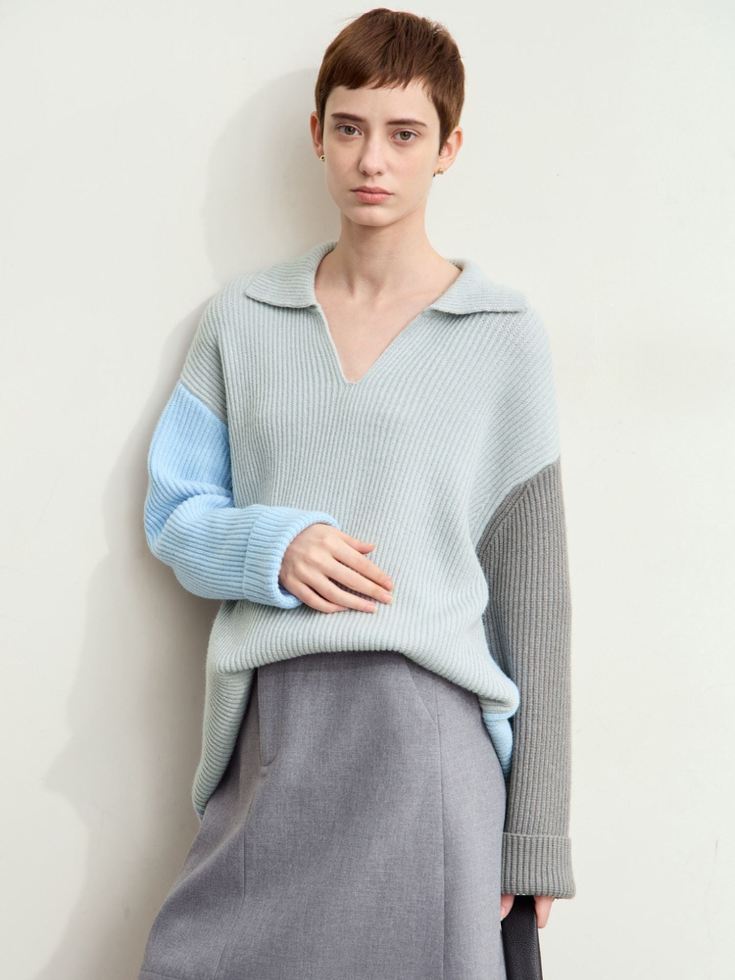 Model i farveblok-strik i lyseblå og grå med krave og lange ærmer.