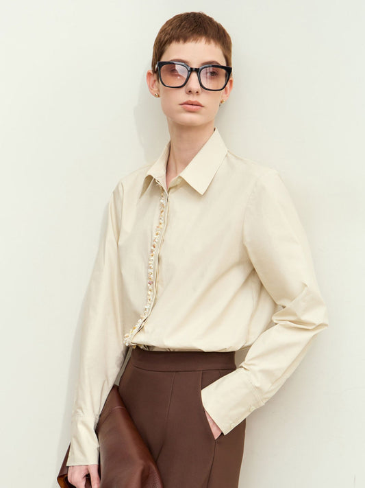 Beige skjorte med perledetaljer og brune bukser, model med solbriller.