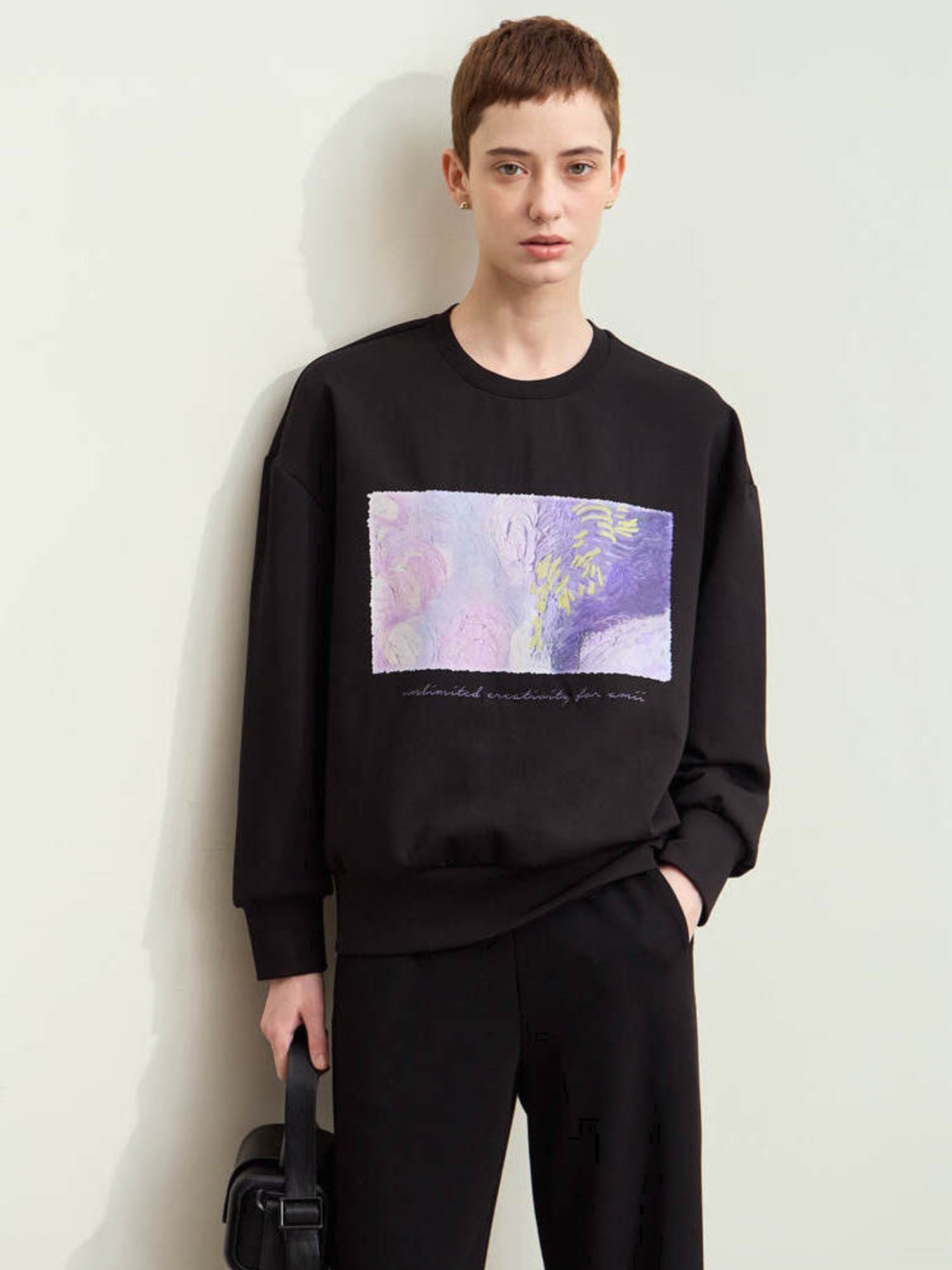 Model i sort sweatshirt med lilla grafisk print foran og sorte bukser.