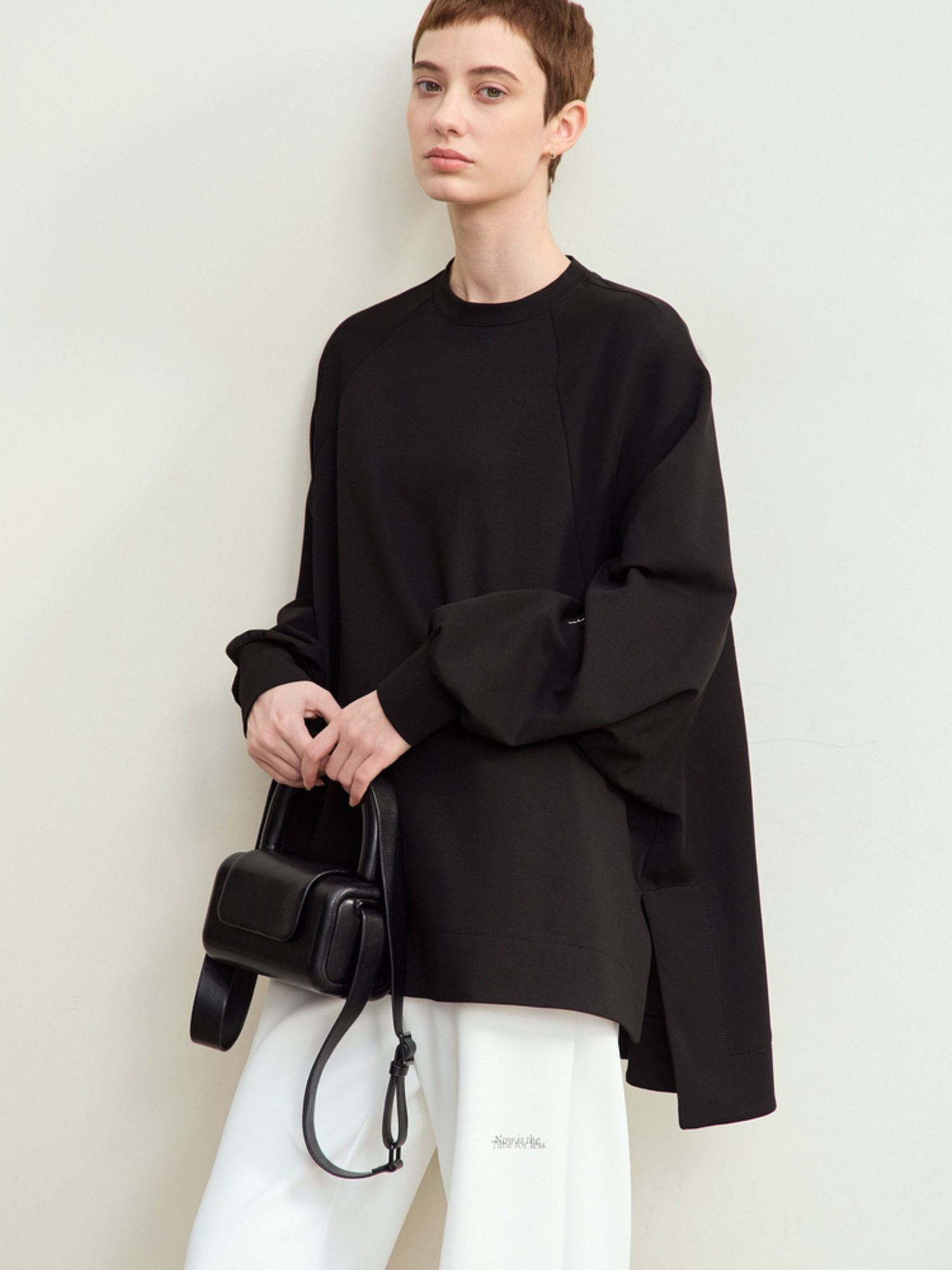 Model iført sort oversized sweatshirt med hvide bukser og sort taske.