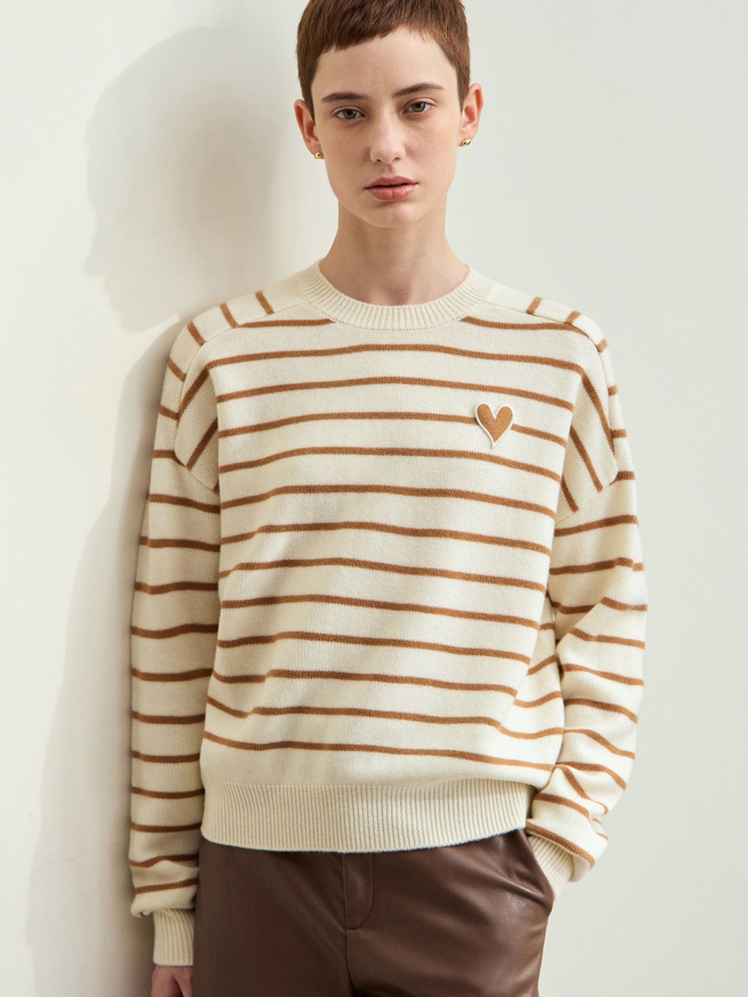 Beige og hvid stribet sweater med brunt hjerteprint, model bærer brune bukser.