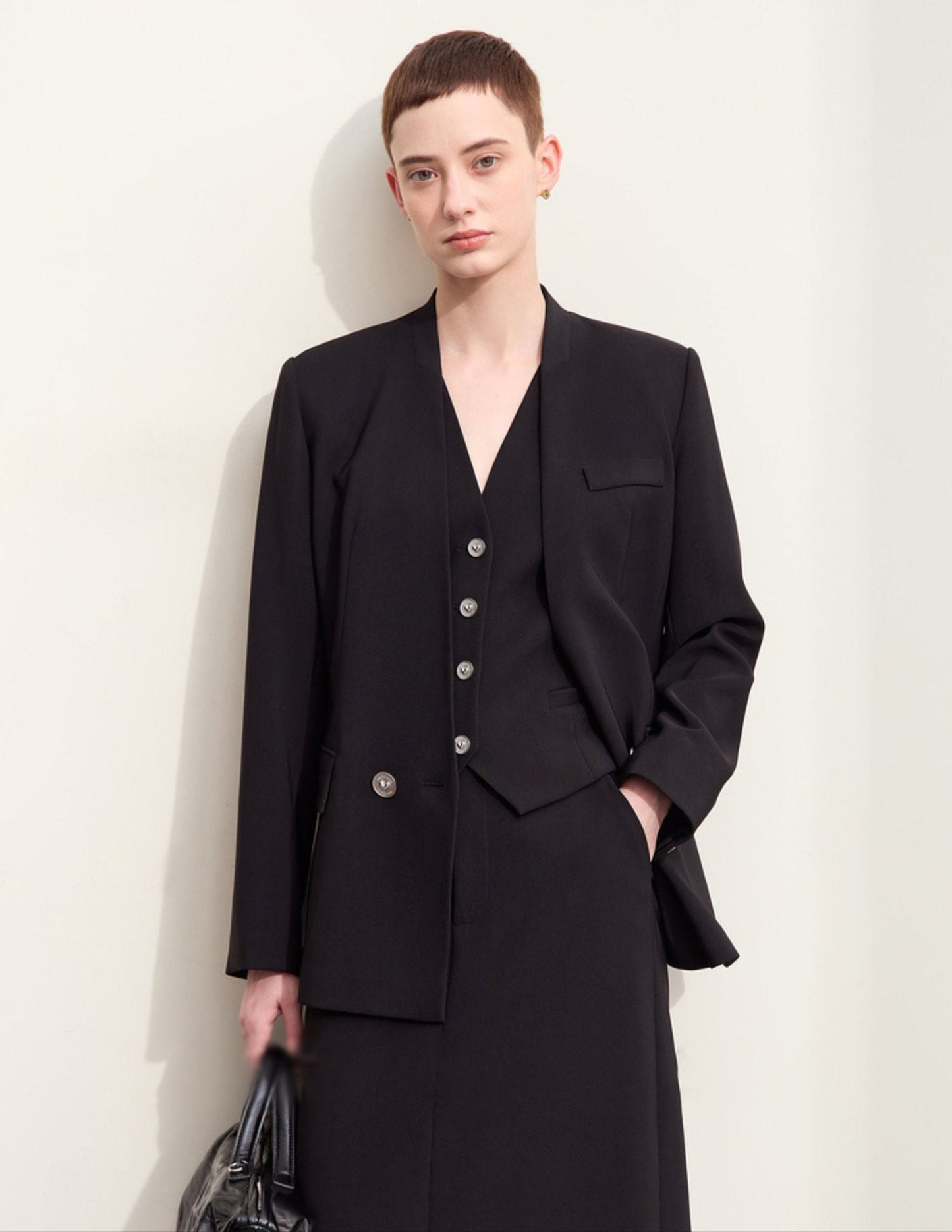 Model iført sort blazer med dyb V-udskæring og matchende nederdel.