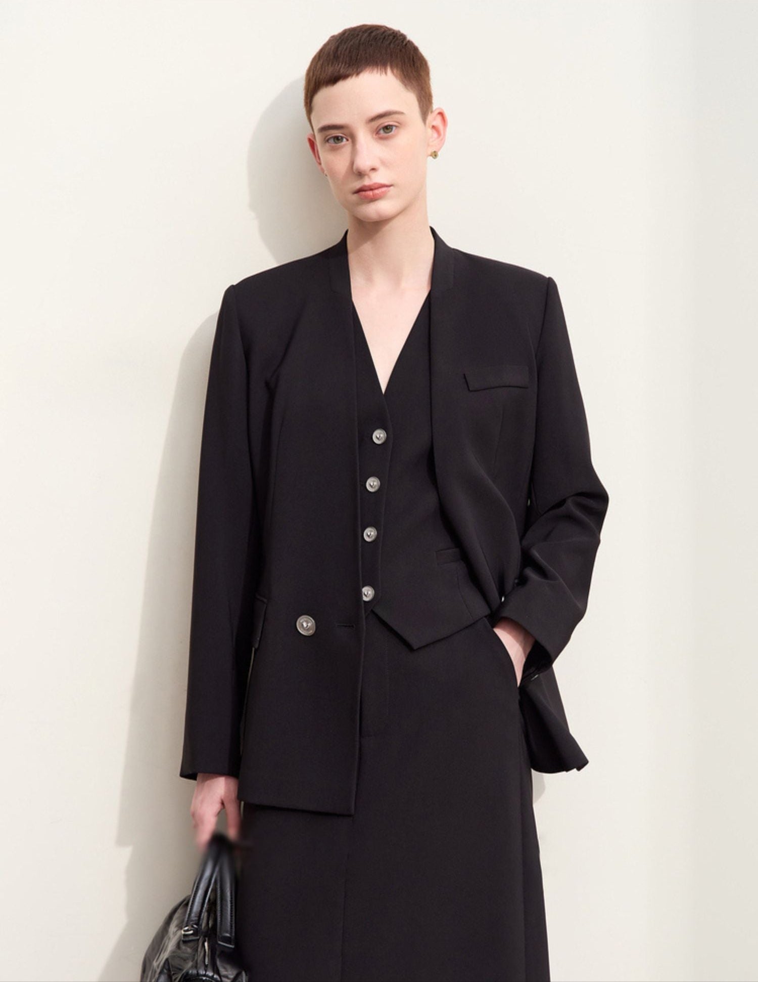 Model iført sort blazer med dyb V-udskæring og matchende nederdel.