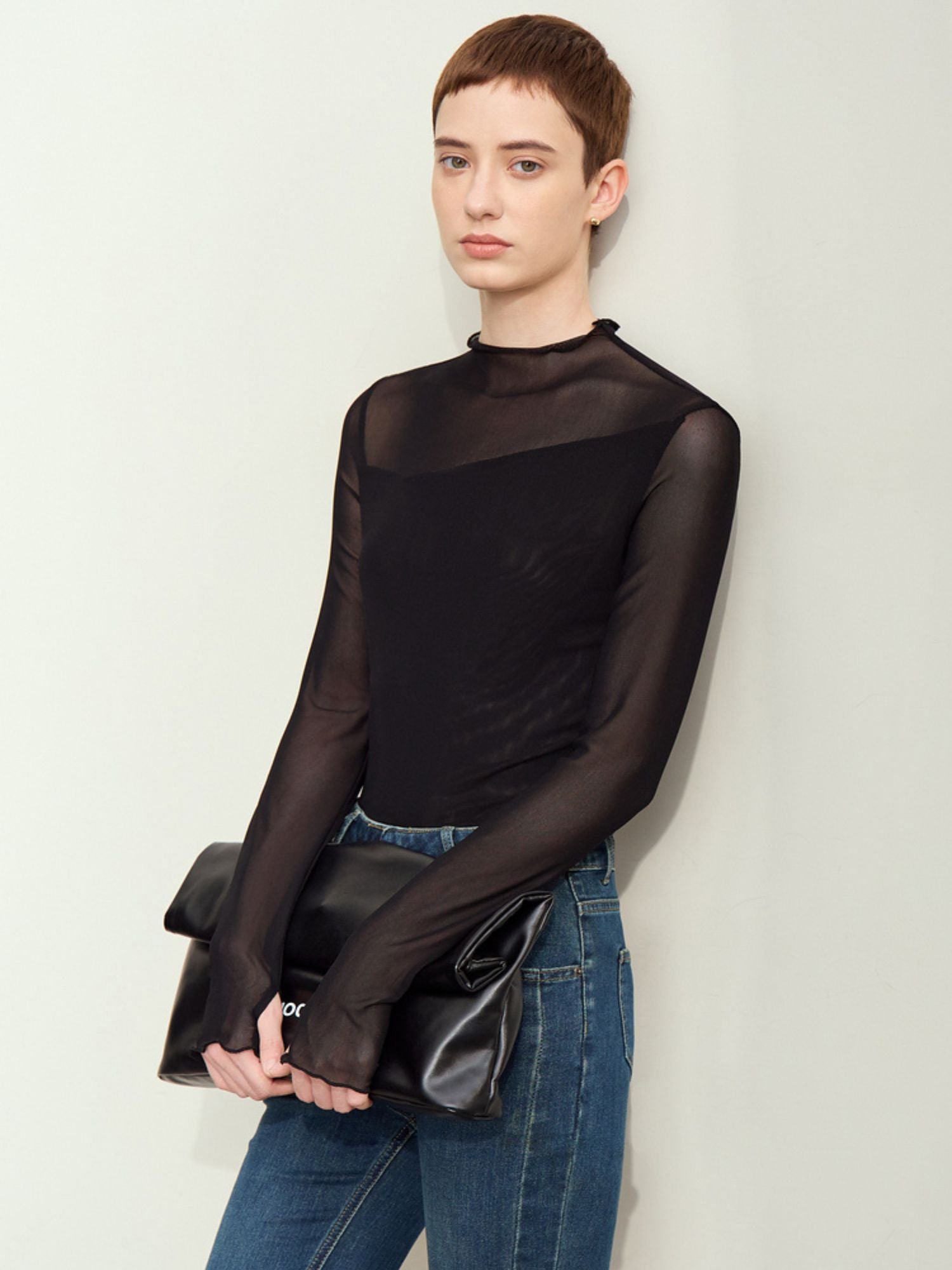 Skrå vinkel af sort mesh-bluse med høj hals, bæres med jeans og clutch.