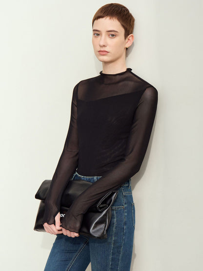 Skrå vinkel af sort mesh-bluse med høj hals, bæres med jeans og clutch.