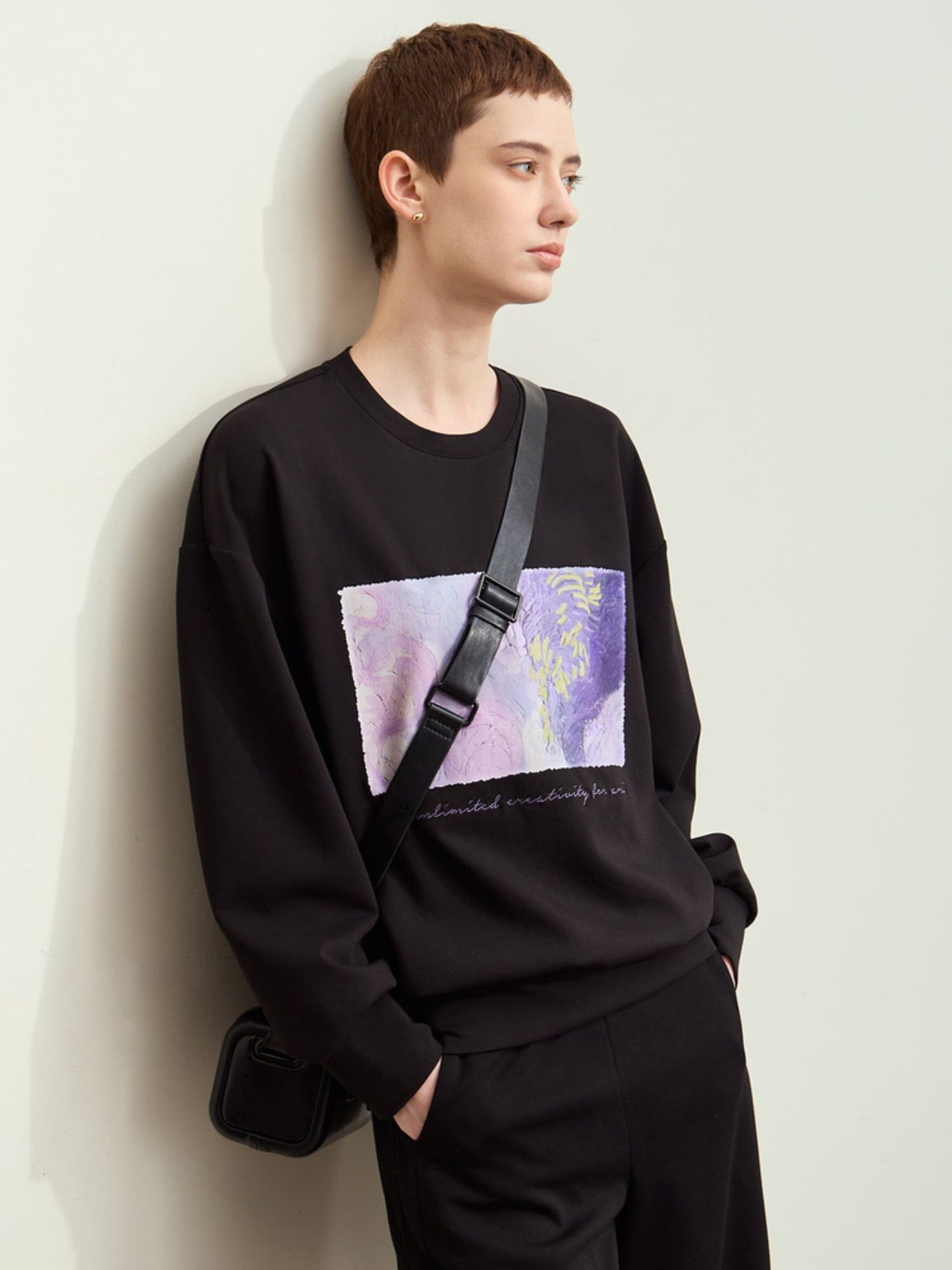 Sidevisning af sort sweatshirt med print, model holder taske.