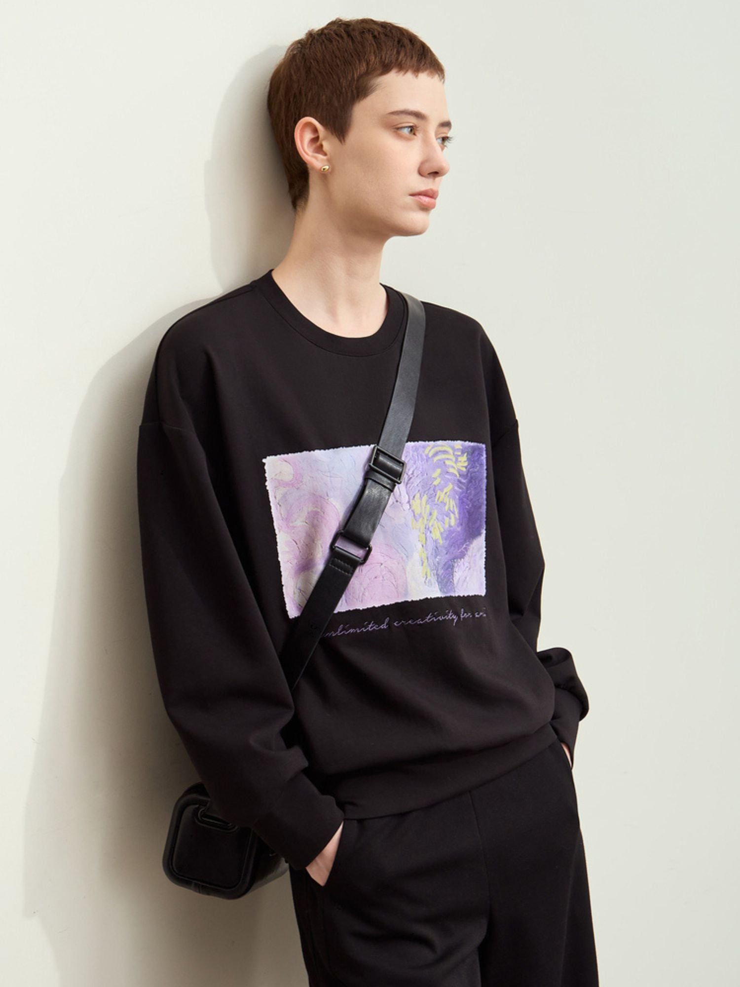 Sidevisning af sort sweatshirt med print, model holder taske.