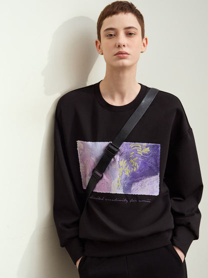 Model står afslappet i sort sweatshirt med kunstnerisk print.
