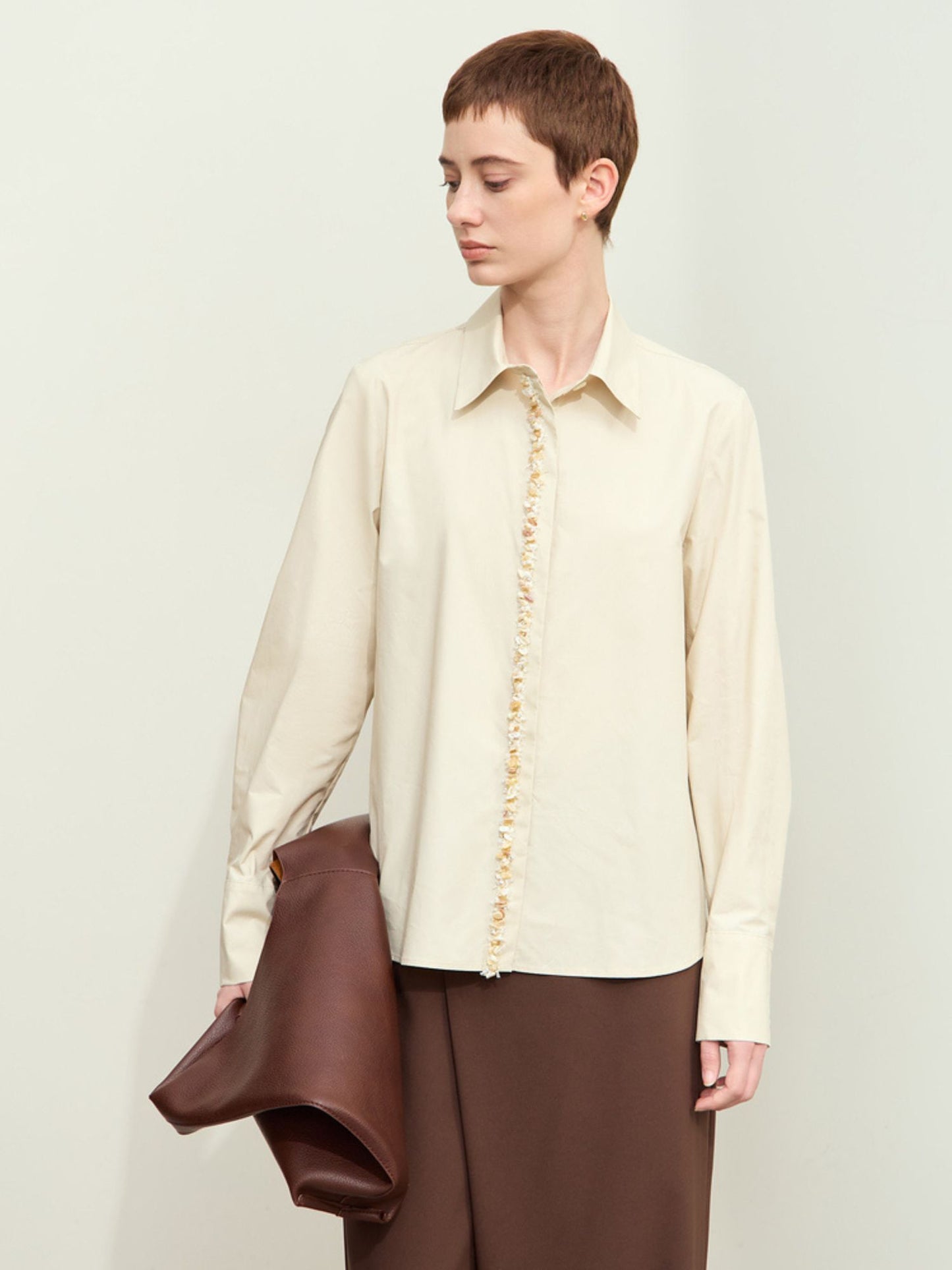 Skrå vinkel af beige skjorte med perledetaljer og solbriller.