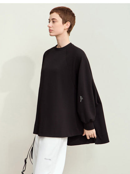 Sidevisning af sort sweatshirt med lange ærmer, båret over hvide bukser.