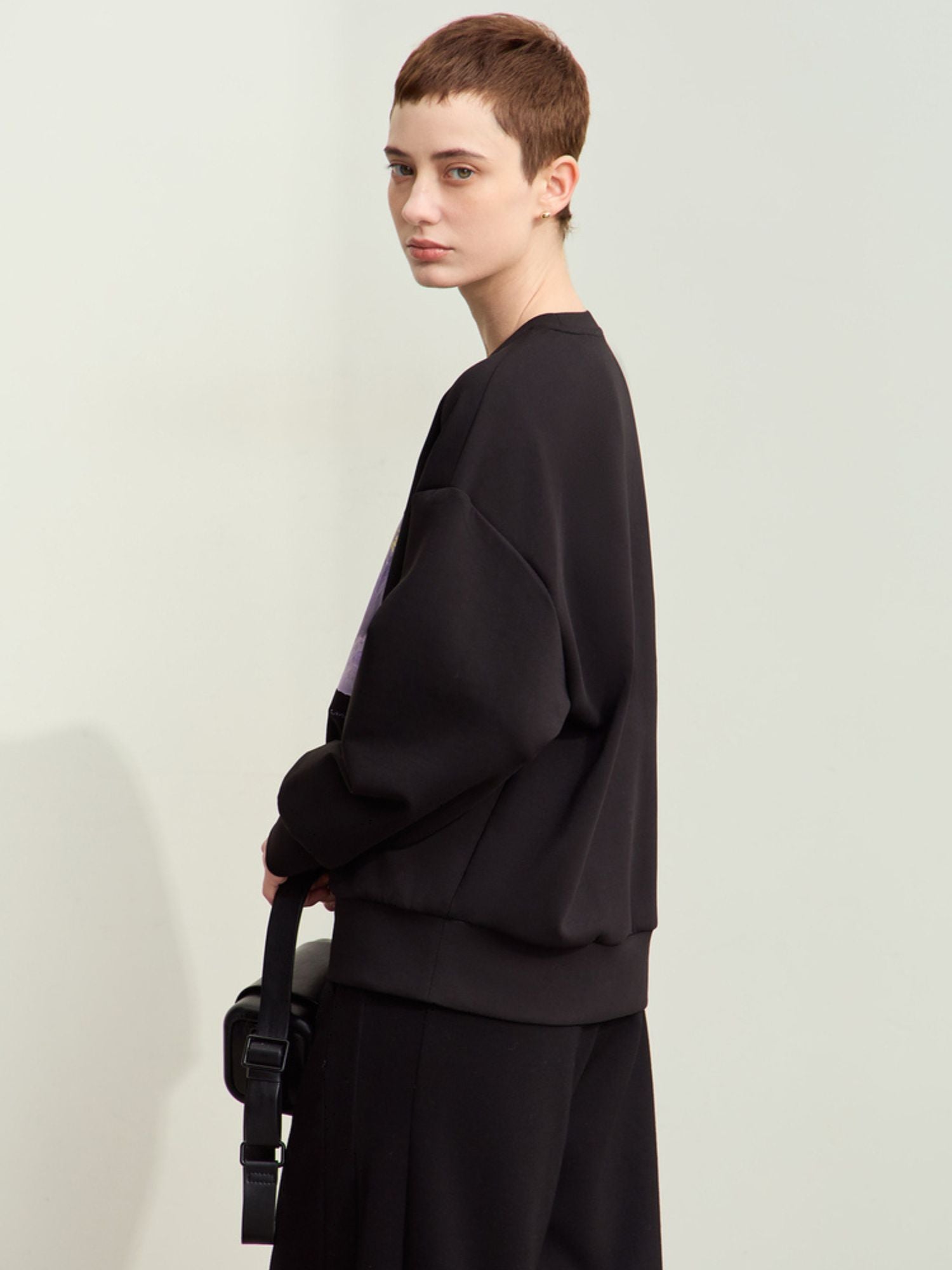 Sidevisning af sort sweatshirt med lilla print og sorte bukser.