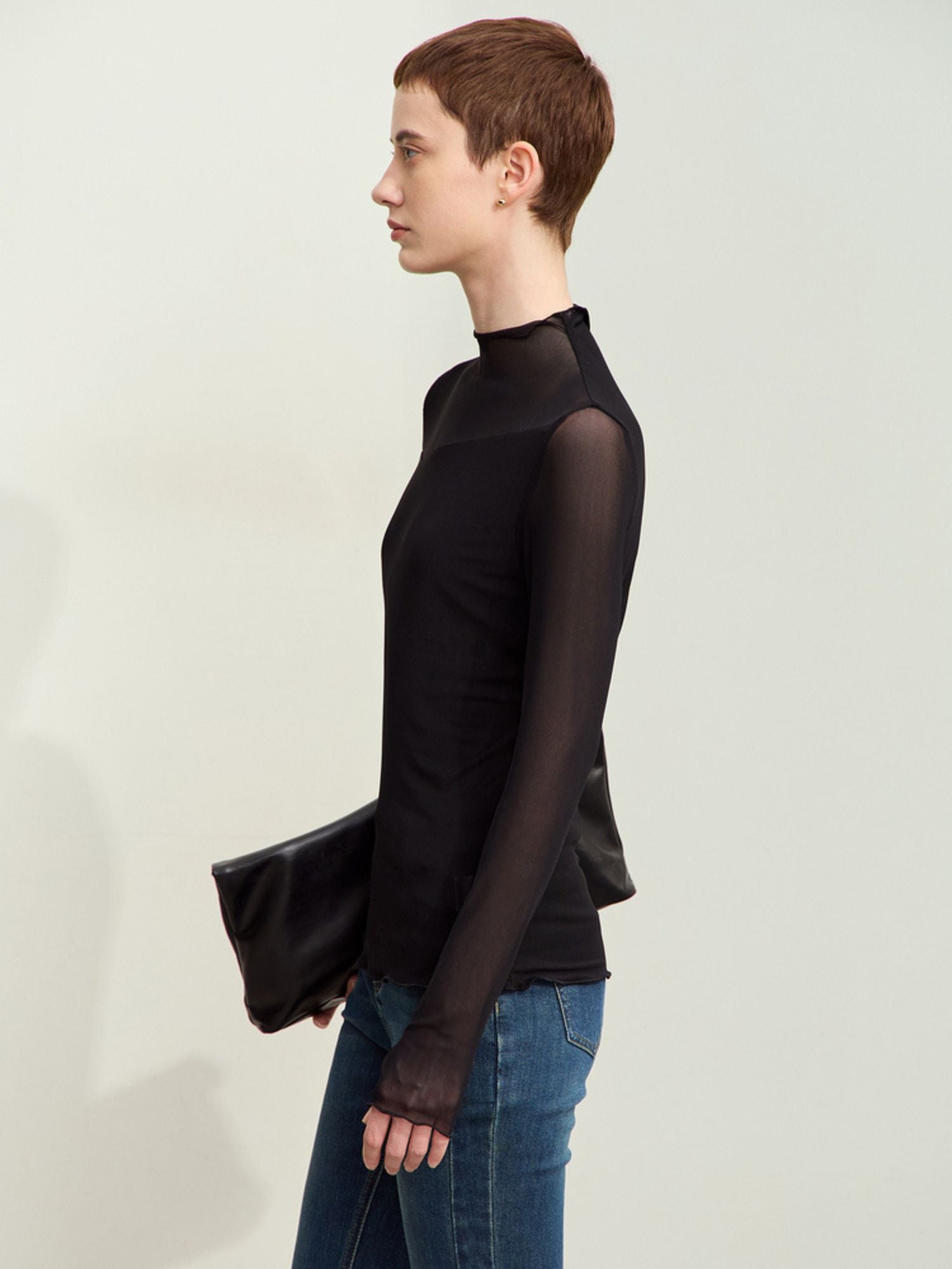 Sort mesh-bluse set i profil, model holder clutch og kigger væk.