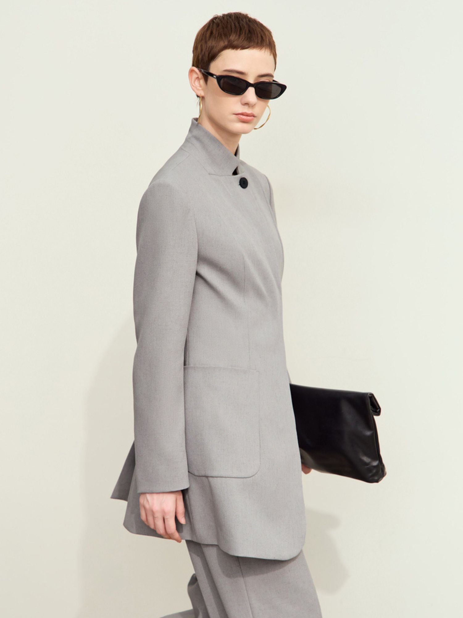 Lysegrå blazer vist fra siden, bæres med sorte accessories.