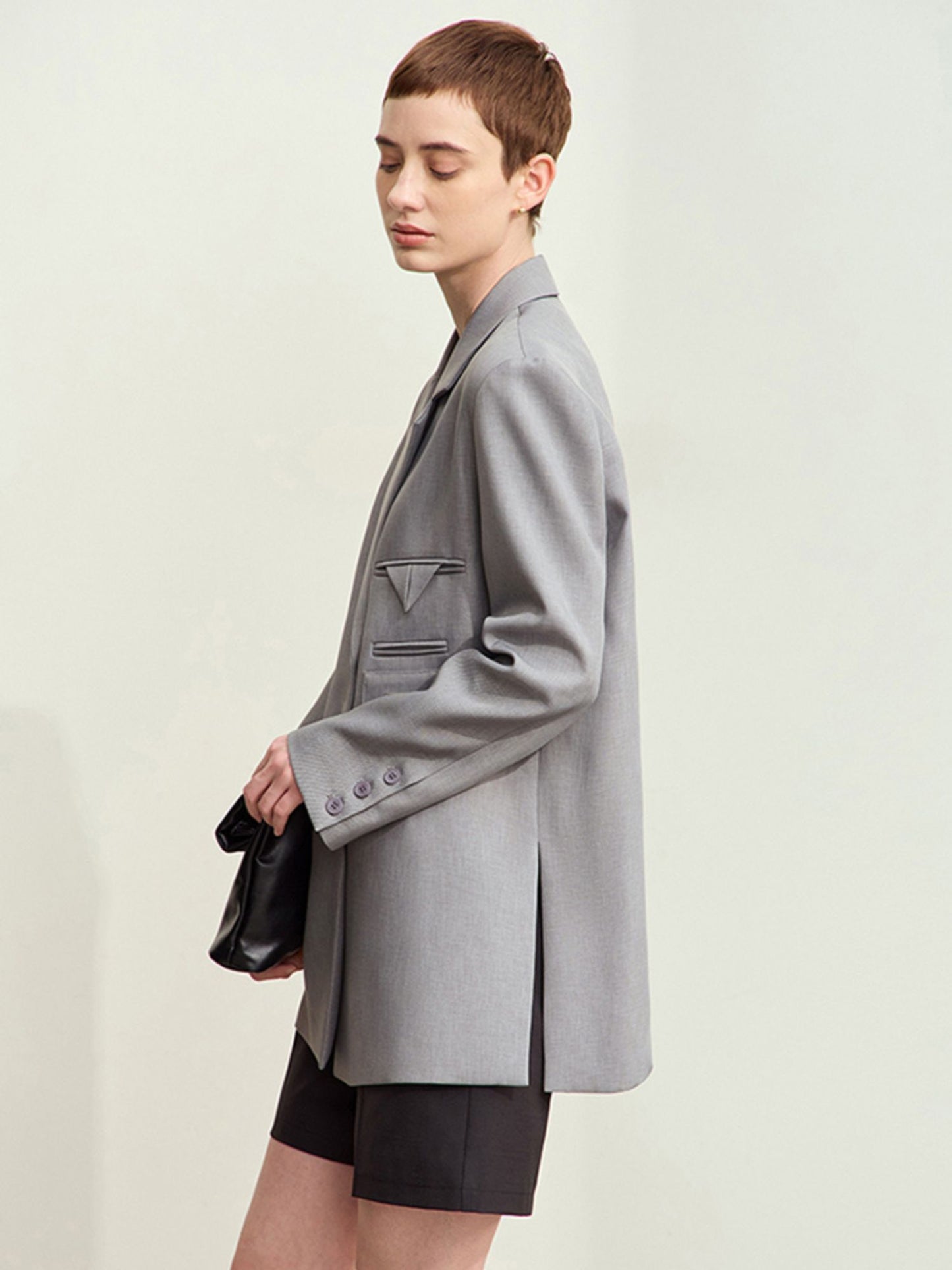 Grå blazer i profil, båret med sort taske og nederdel.