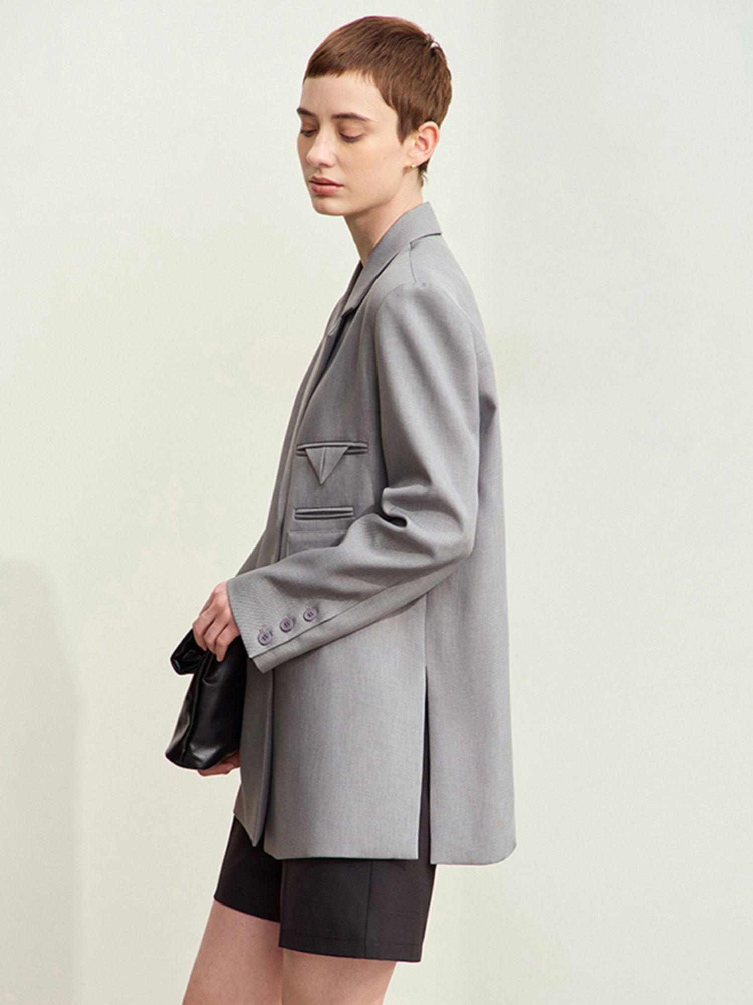 Grå blazer i profil, båret med sort taske og nederdel.