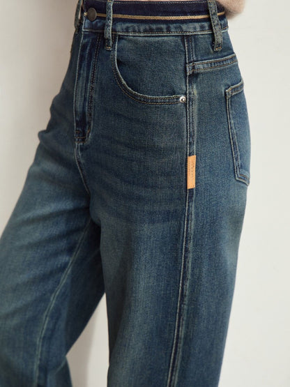 Model i brun top og mørkeblå jeans med hænderne i lommerne.