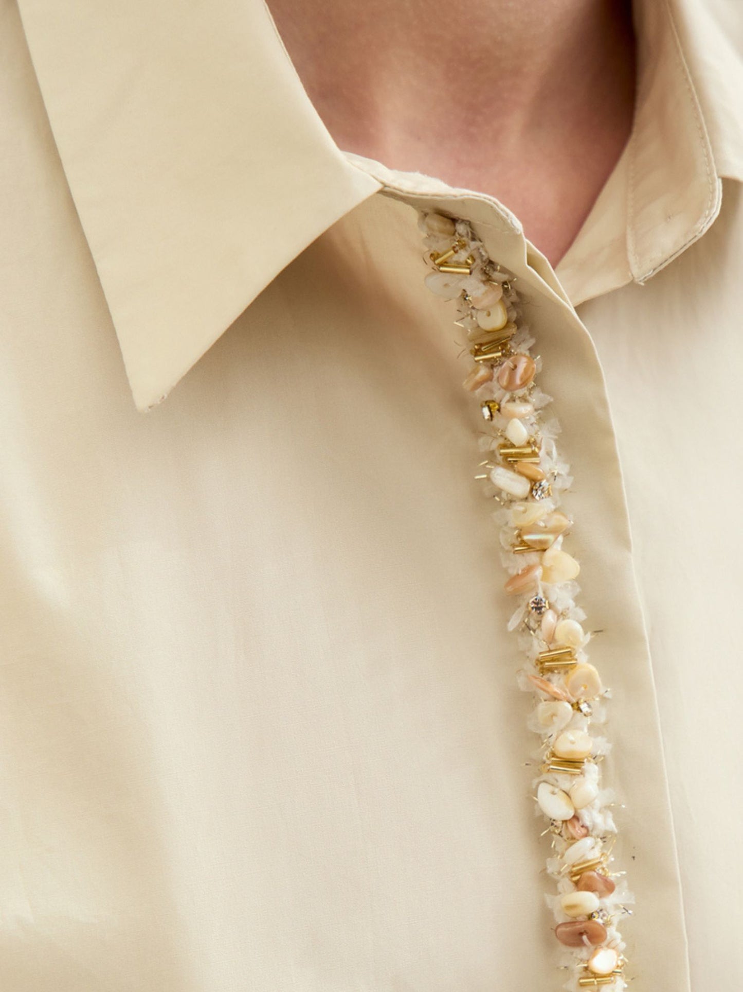 Beige skjorte med perler, model står oprejst med hånden i lommen.