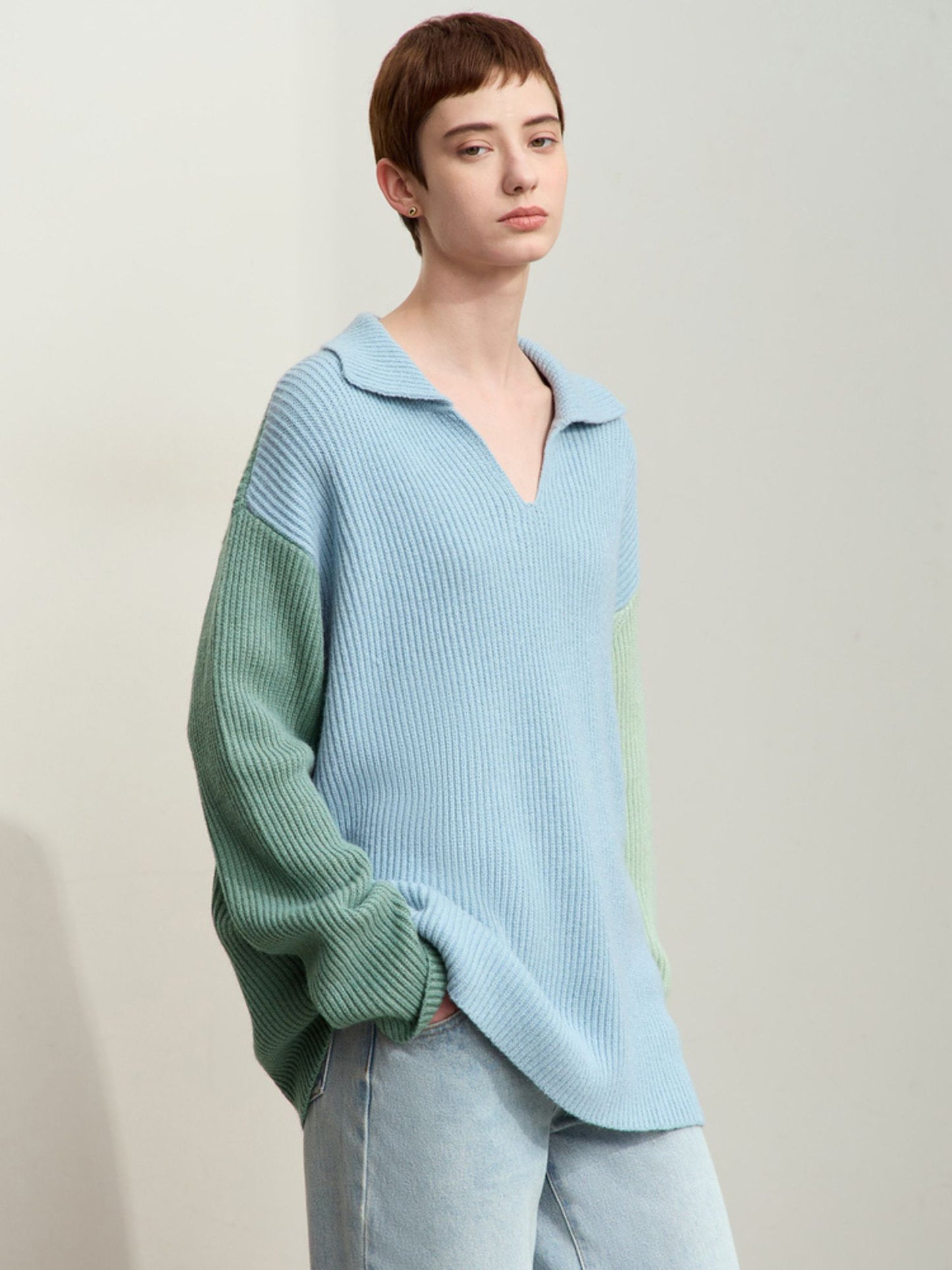 Model sidder i lysegrøn og blå striktrøje med hånd på hovedet.