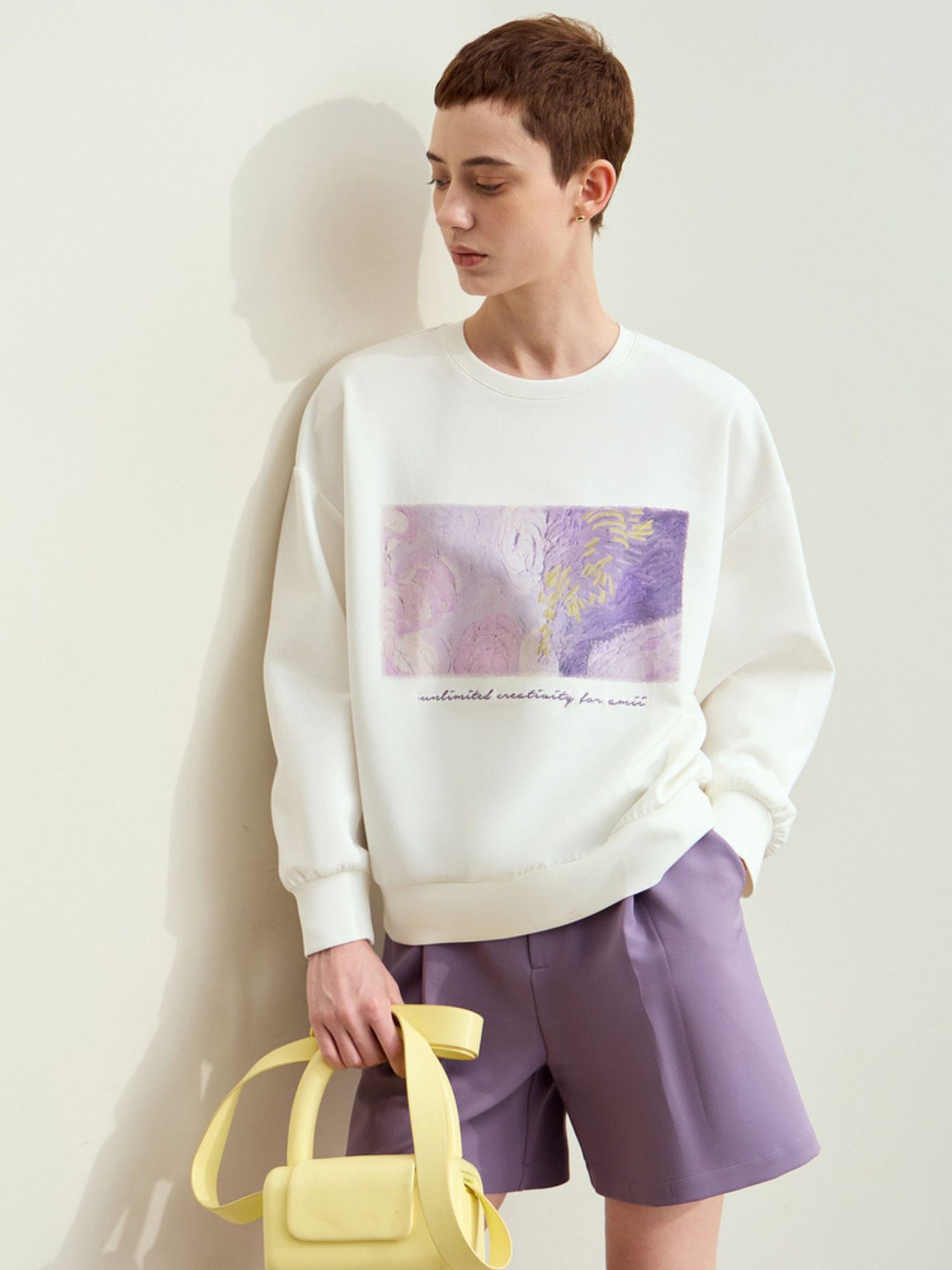 Hvid sweatshirt med kunstprint og model der holder gul taske.