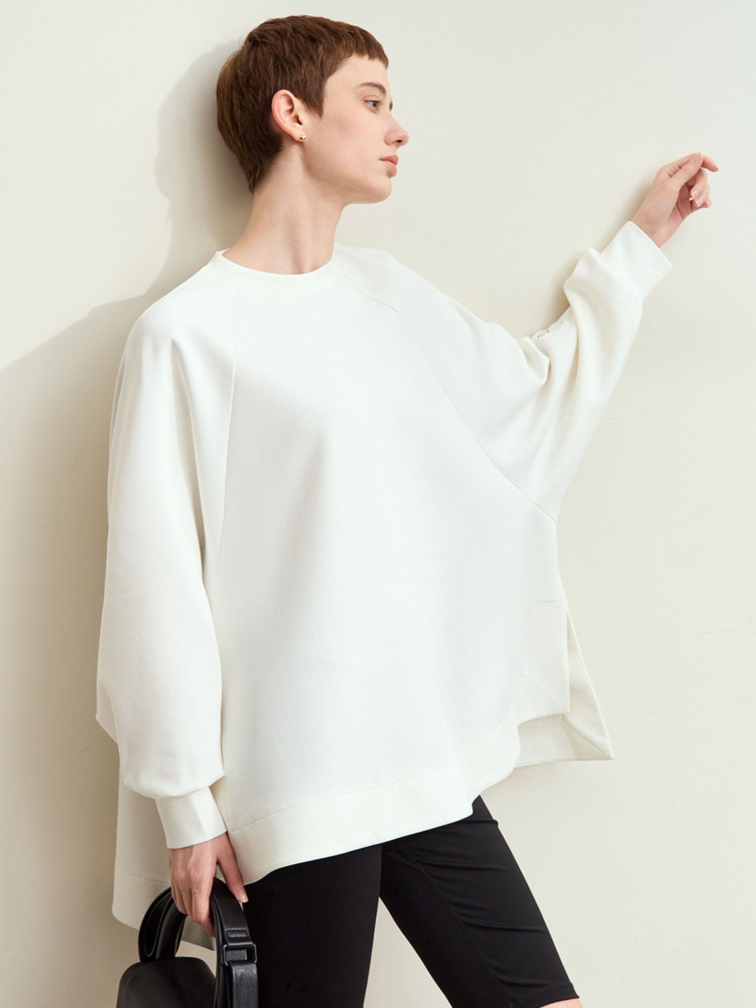 Sidevinkel af hvid sweatshirt med bred silhuet og albuelange ærmer.